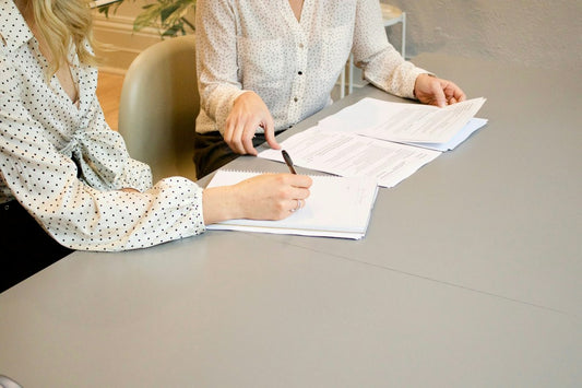 woman signing on white printer paper beside woman about to touch the documents - Photo by Gabrielle Henderson on Unsplash